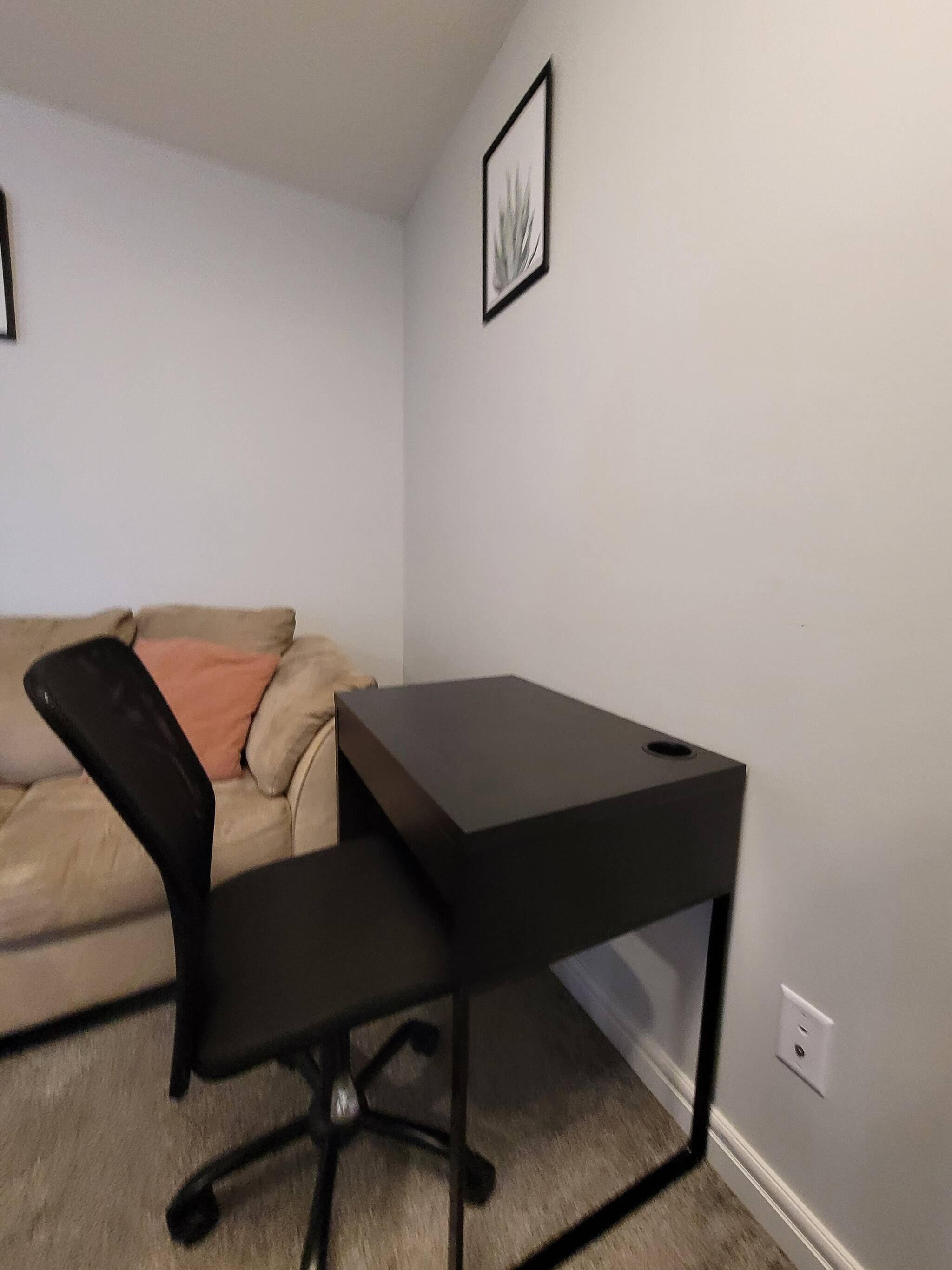 A room with a black desk, a beige sofa, and a framed picture on the wall.