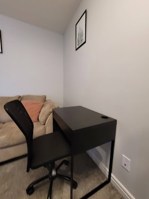 Une pièce avec un bureau noir, un canapé beige et un tableau encadré accroché au mur.