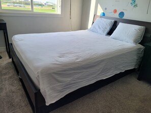 Una cama bien tendida con sábanas blancas, un cabecero de madera oscura y un mural con motivos celestiales.