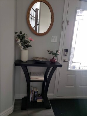 A hallway with a console table, a mirror, a vase with flowers, a door with a handle, and a window. - Room-charming Home in North Edmonton (Edmonton)