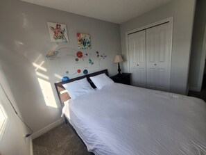 Une chambre à coucher comprenant un lit, une table de chevet, une lampe, une armoire et des œuvres d’art mural représentant des planètes et une girafe.