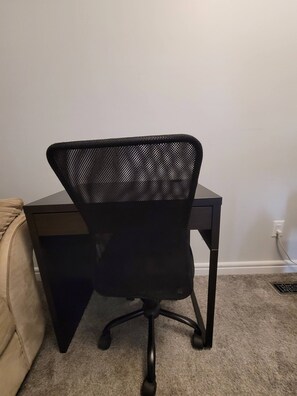 A black office chair with a mesh backrest and wheels, positioned in front of a desk. - Room-charming Home in North Edmonton (Edmonton)