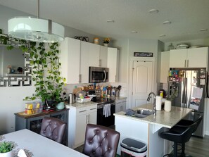 A modern kitchen with white cabinets, a microwave, a sink, and a dining area with two chairs. - Room-charming Home in North Edmonton (Edmonton)