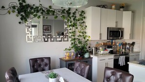 A dining area with a table, chairs, a plant, and a kitchen in the background.