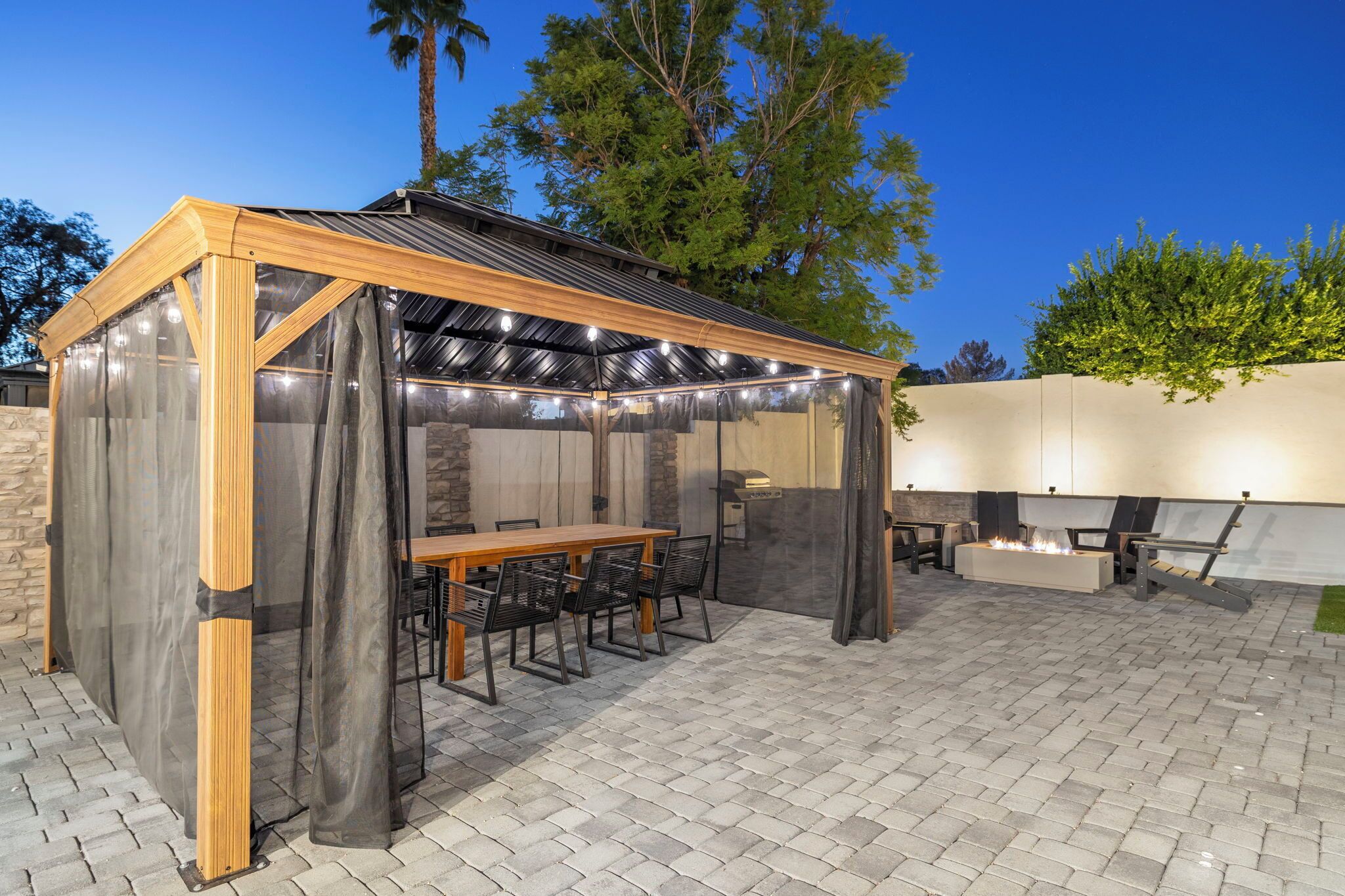 A covered outdoor seating area with a table and chairs, a grill, and a pergola with string lights.
