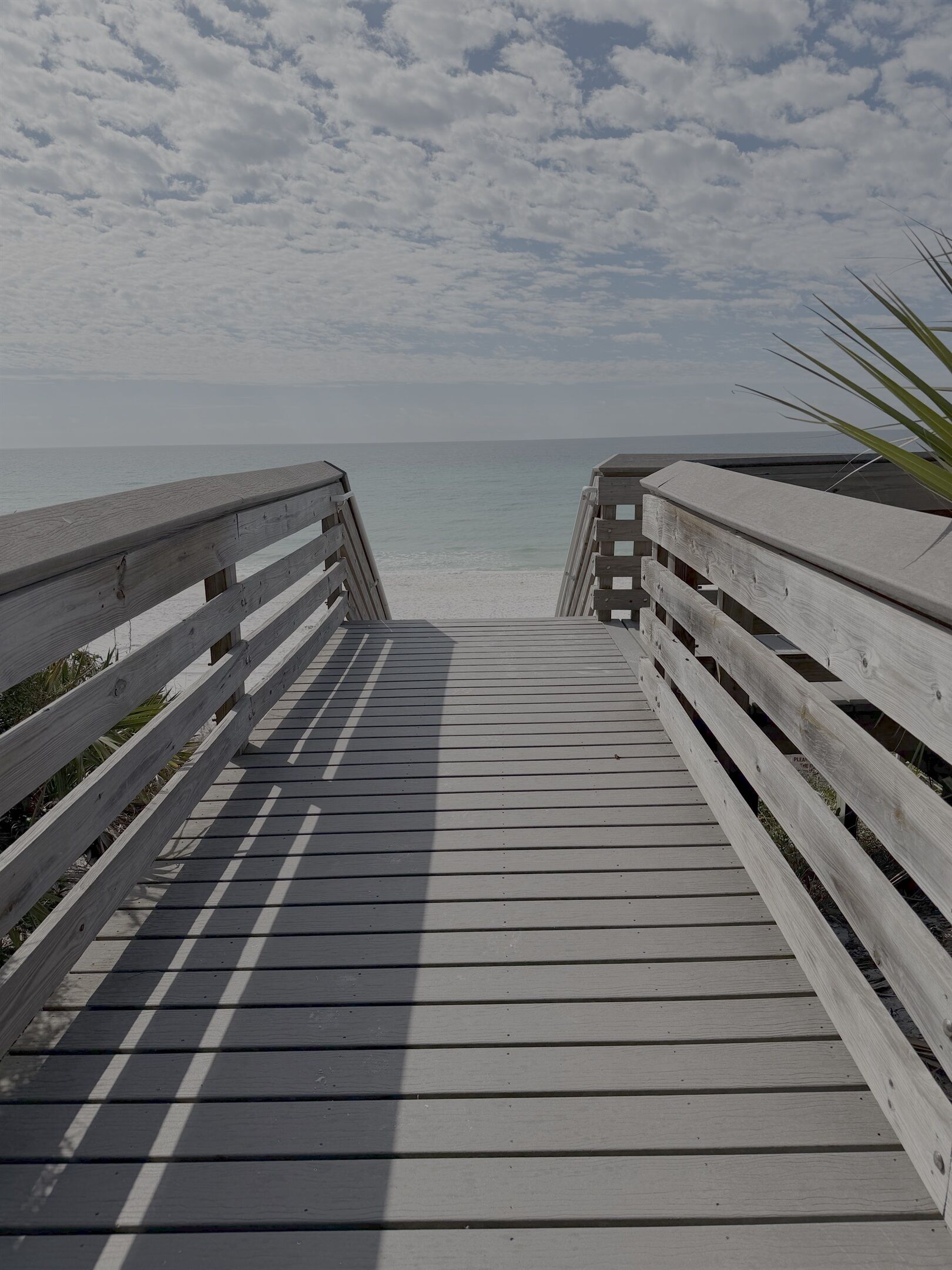 A wooden boardwalk leading to a beach with a clear view of the ocean.