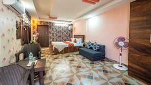 Una habitación de hotel con una cama, un sofá, una mesa de comedor, un ventilador y un adorno de pared.