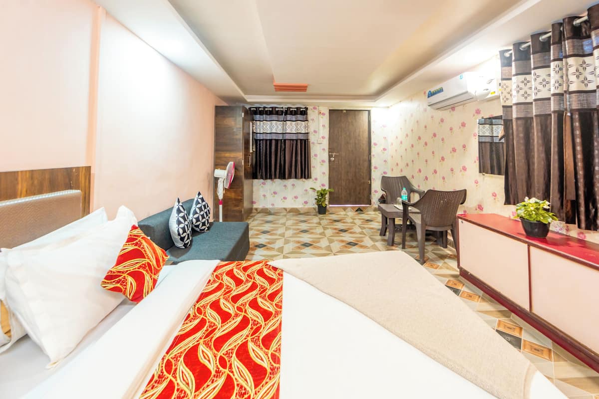 A hotel room with a bed, a desk, a chair, a small table, and a potted plant.
