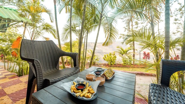 Una mesa con una porción de papas fritas y salsas para mojar, una silla de mimbre y vistas a palmeras y un paisaje lejano.