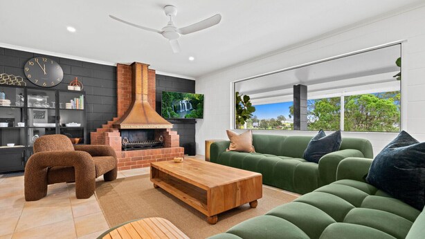 Una sala de estar moderna con chimenea, sofá verde, mesa de centro de madera y televisor montado en la pared.