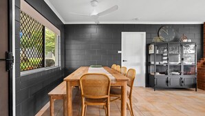 Un comedor con una mesa de madera y sillas de mimbre, una pared de ladrillo negro, una puerta blanca y un armario con puertas de cristal.