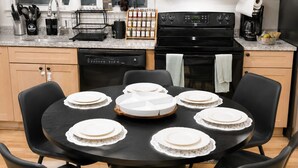 A modern kitchen with a round dining table, black chairs, a built-in oven, and a microwave above the counter. - Brand New Spacious Family Friendly Home near Boston (Somerville)