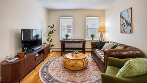 A living room with a TV, sofa, coffee table, and a decorative rug. - Brand New Spacious Family Friendly Home near Boston (Somerville)
