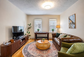A living room with a TV, sofa, coffee table, and a decorative rug. - Brand New Spacious Family Friendly Home near Boston (Somerville)