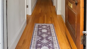 A hallway with wooden flooring, a patterned rug, a wooden door with a glass panel, and a ceiling light fixture. - Brand New Spacious Family Friendly Home near Boston (Somerville)