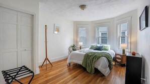 A bedroom with a bed, bedside tables, a lamp, a floor lamp, a chair, and a wardrobe. - Brand New Spacious Family Friendly Home near Boston (Somerville)