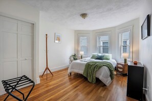 A bedroom with a bed, bedside tables, a lamp, a floor lamp, a chair, and a wardrobe. - Brand New Spacious Family Friendly Home near Boston (Somerville)