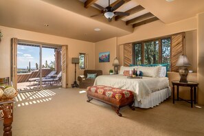 A bedroom with a large bed, a window with a view, a ceiling fan, and a small table. - NEW 6BR Carefree Estate with Views | Tennis, Pickleball, Pool, Infinity Spa, Golf & Views (Carefree)