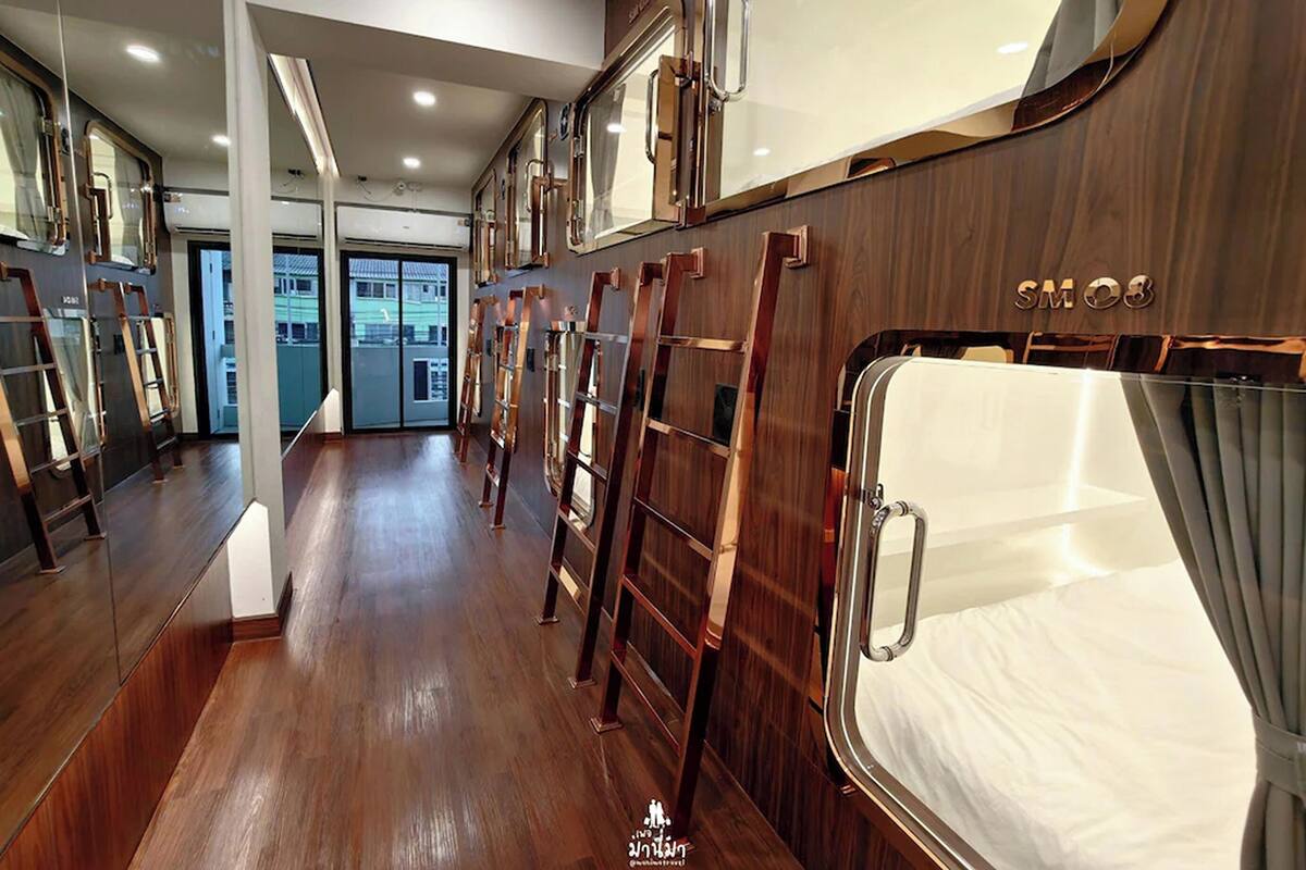 Un pasillo con suelo de madera, paredes espejadas y una cama con estructura metálica.