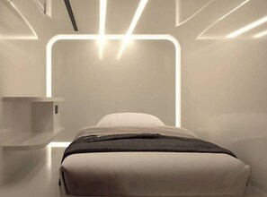 A modern, minimalist bedroom with a bed, bedside table, and a wall-mounted light fixture. - The Rich Cafe & Hostel (Pattaya)
