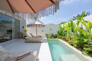 A poolside area with a lounge chair, a cushioned bench, a small table, and a statue. - Casa Suka Villa by Pertama Stay (Ungasan)
