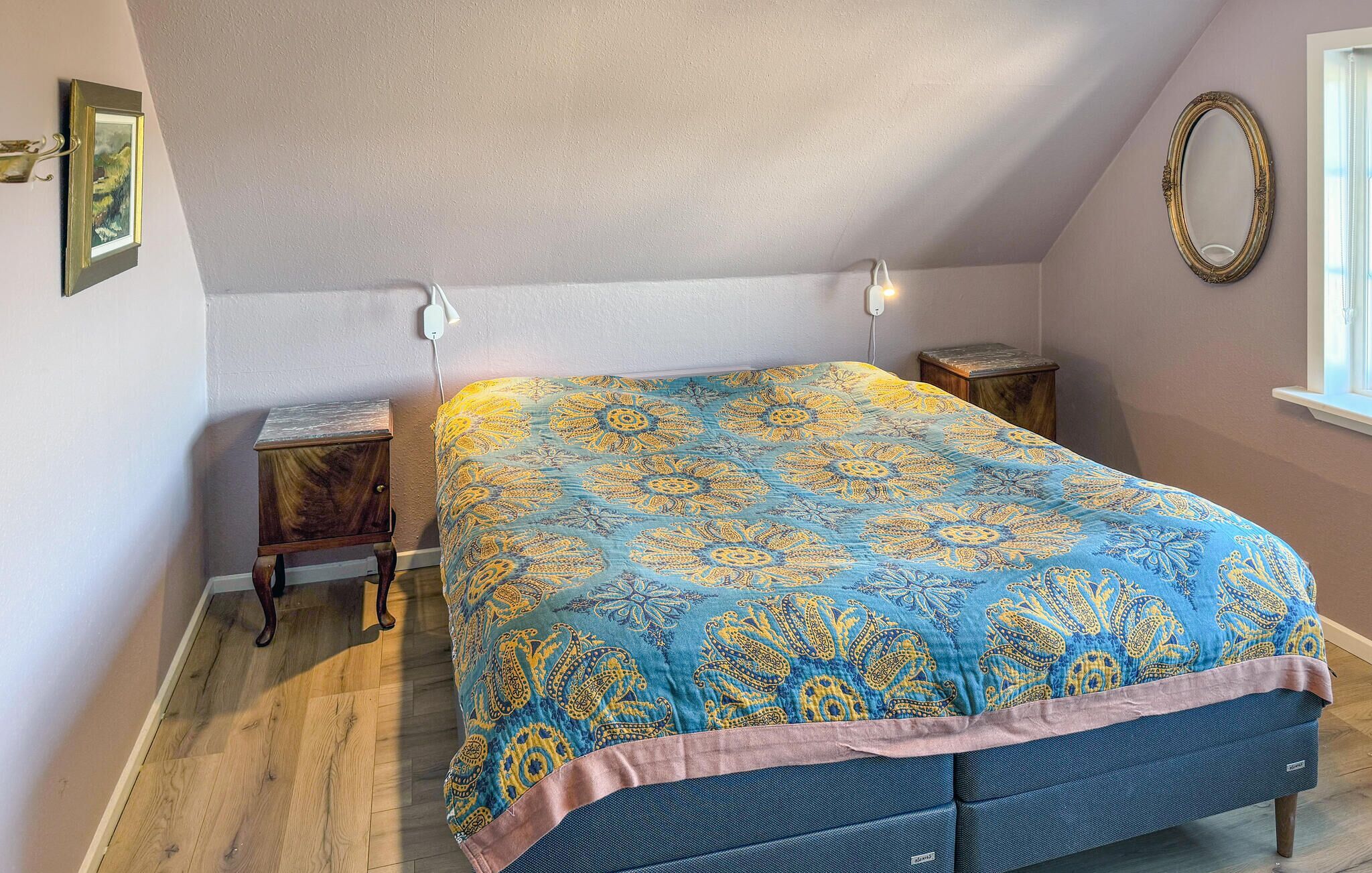 A bedroom with a bed, a nightstand, a dresser, a wall-mounted mirror, and a window.