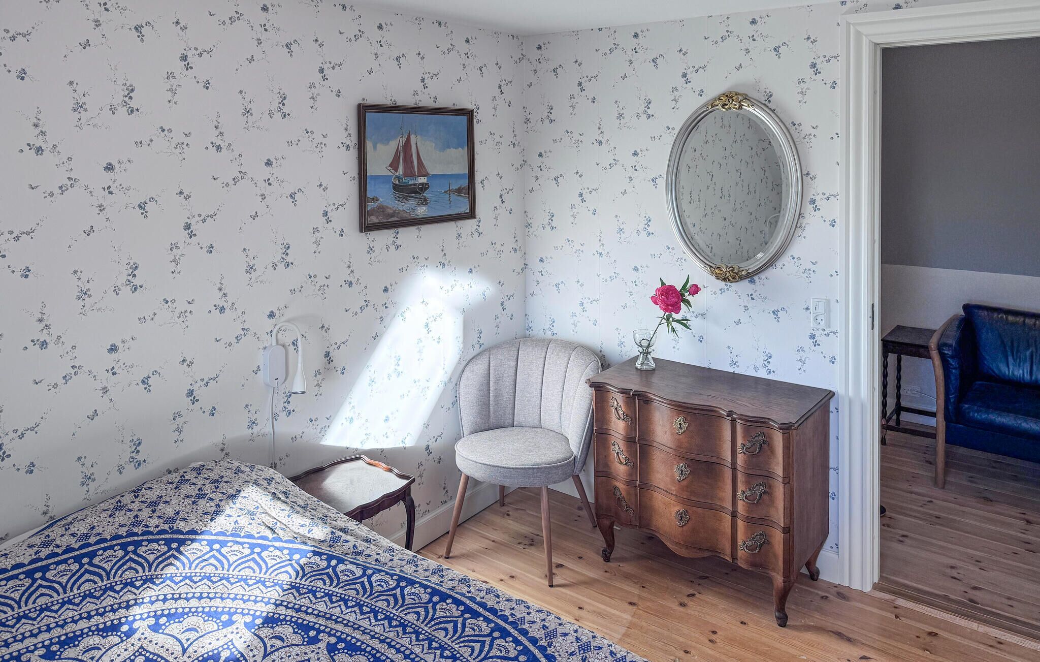 A bedroom with a bed, a chair, a dresser, a mirror, and a painting on the wall.