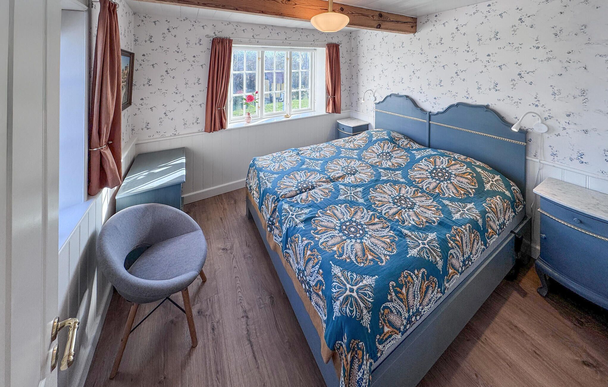 Une chambre à coucher comprenant un lit, une chaise, une commode, une fenêtre avec des rideaux et un radiateur.