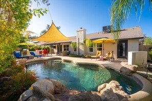 A swimming pool with lounge chairs and umbrellas, a covered patio, and a house with a chimney. - Desert Ridge Family new Renovated with Spa and Pool (Phoenix)