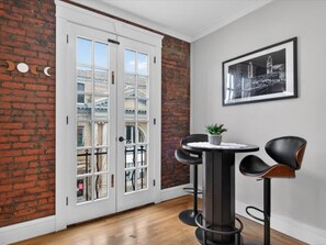 A room with a brick wall, a white door, a round table with chairs, and a framed picture on the wall.