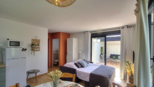 A bedroom with a bed, a desk, a chair, a microwave, and a sliding glass door leading to a balcony.
