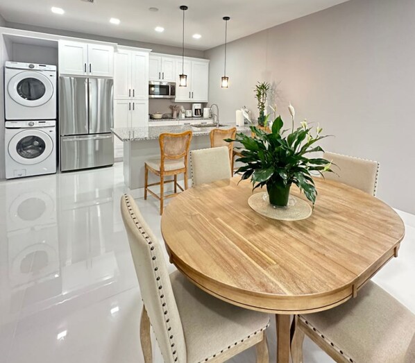 A modern kitchen with stainless steel appliances, a dining area with a round wooden table, and white cabinetry.