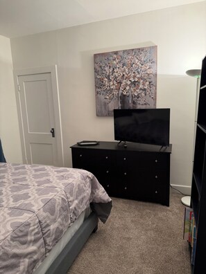 A bedroom with a bed, a dresser, a TV, and a painting on the wall.