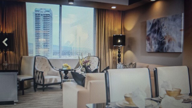 A hotel room with a large window, a sofa, a chair, a table, and a lamp.