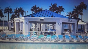 A poolside building with a blue roof, surrounded by lounge chairs and palm trees.