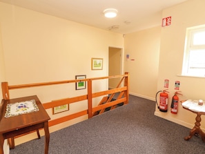 A hallway with a wooden railing, framed pictures on the wall, a small table with a lace tablecloth, and two fire extinguishers mounted on the wall. - MACMATHUNA, family friendly, with a garden in Kilrush, County Clare (Kilrush)