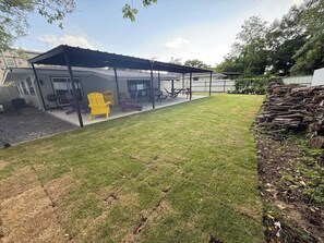 Un espacio al aire libre cubierto con una mesa y sillas de patio, un pequeño edificio con ventana, y una pila de leña.