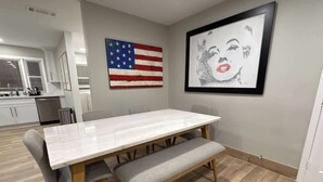 Een eethoek met een witte tafel, houten stoelen en een bank. Een Amerikaanse vlag en een lijst met kunstwerk hangen aan de muur.