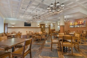 A spacious dining area with wooden tables and chairs, a high ceiling with decorative moldings, and a chandelier. - Ski-Lift Next Door, 6 Guest, 2BR 2BA Pool & Spa, Sauna, Gym, Restaurant, Wi-Fi (Brian Head)