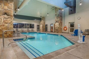 An indoor swimming pool with stone walls, a lifeguard stand, and a view of the mountains through large windows. - Ski-Lift Next Door, 6 Guest, 2BR 2BA Pool & Spa, Sauna, Gym, Restaurant, Wi-Fi (Brian Head)