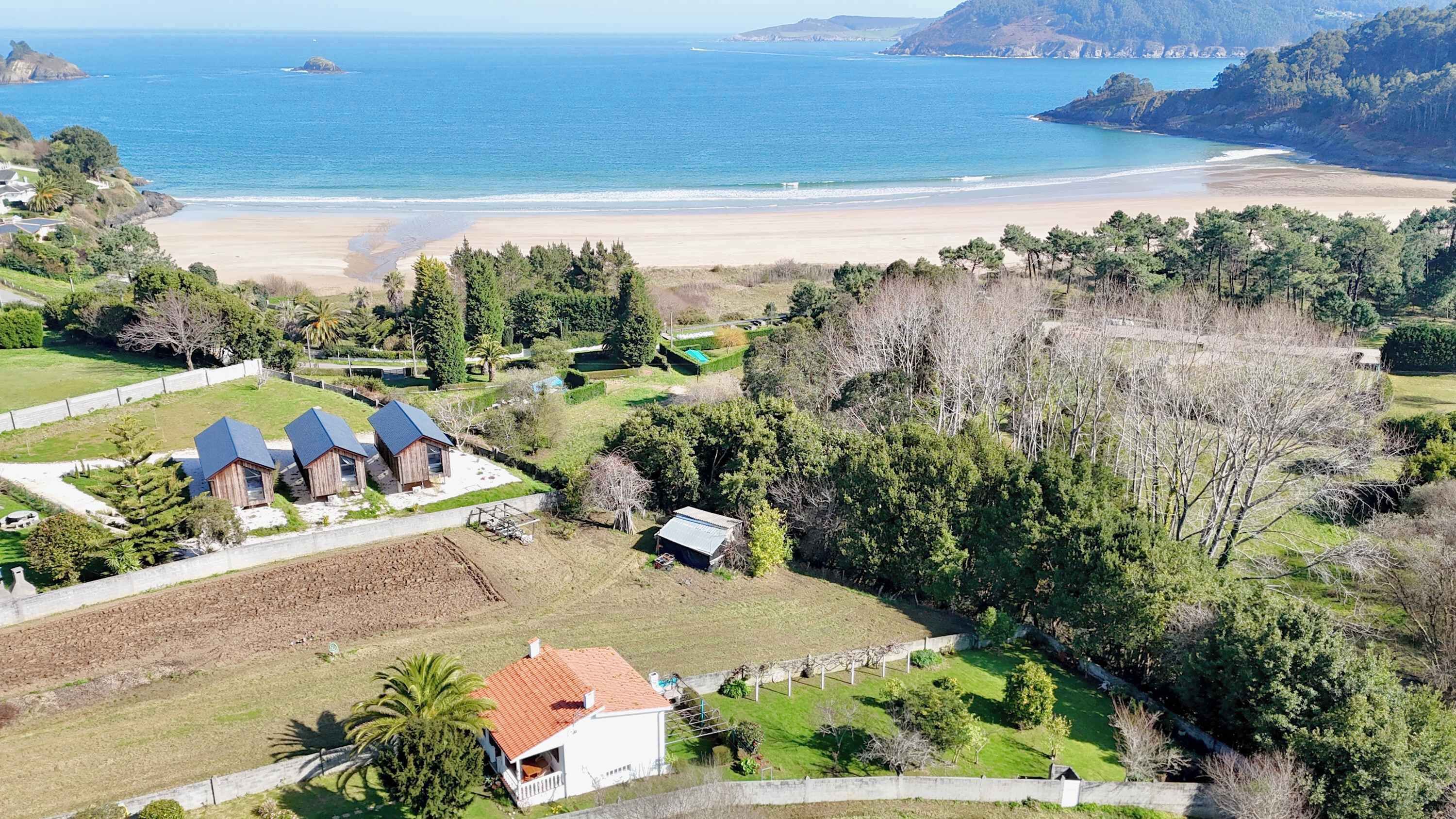 A coastal property with a beach view, a fenced garden, and several buildings with blue roofs.