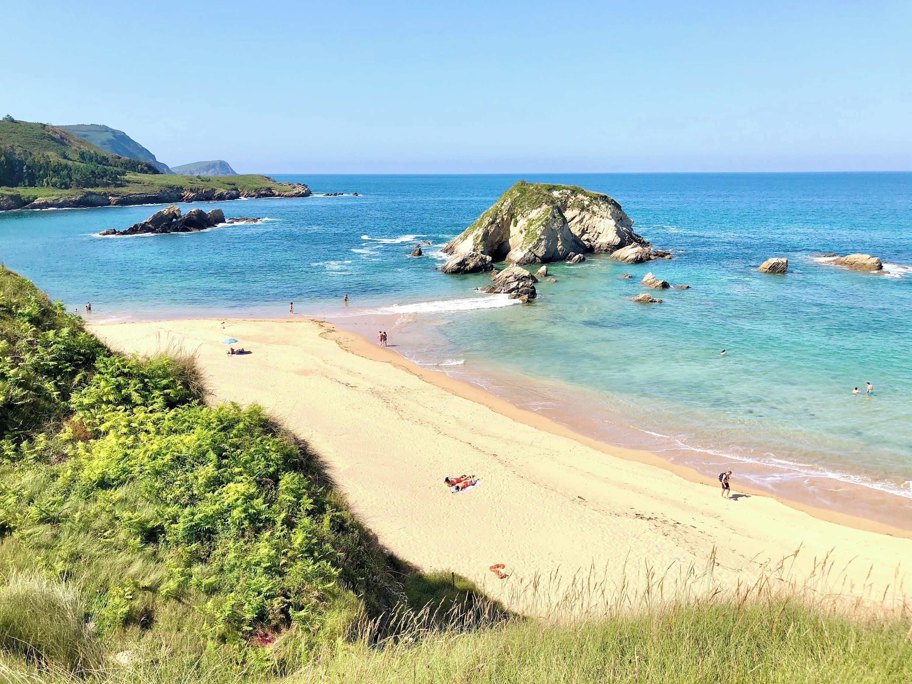 Ein Strand mit klarem türkisfarbenem Wasser, einem Sandstrand und Felsformationen.