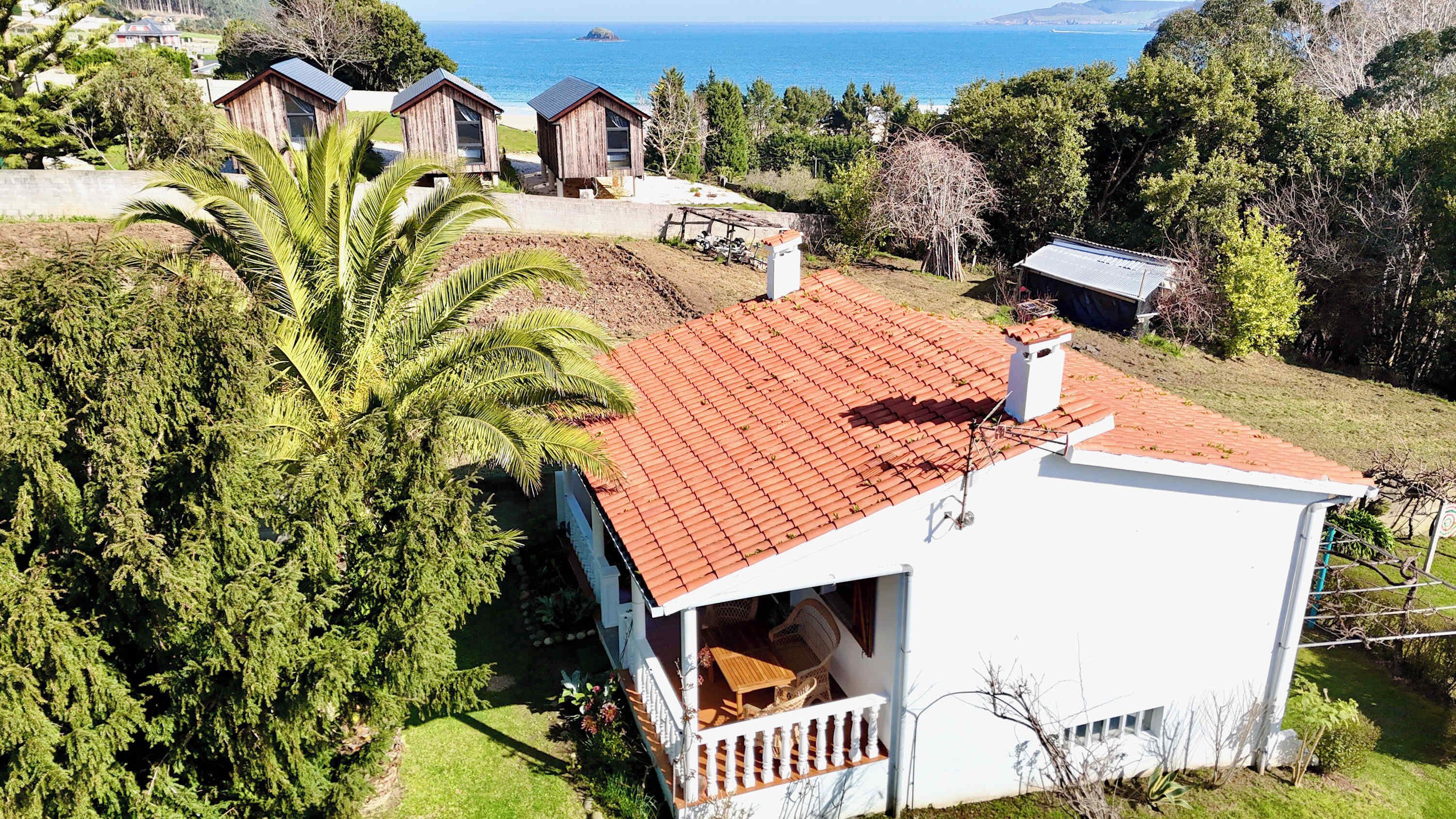 A white house with a red-tiled roof, a balcony, and a view of the sea.