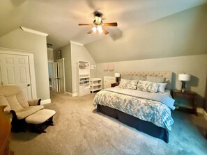 A bedroom with a bed, a chair, a ceiling fan, a wardrobe, and a desk.