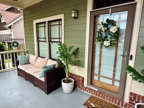 A porch with a wicker sofa, a potted plant, and a door with a wreath.
