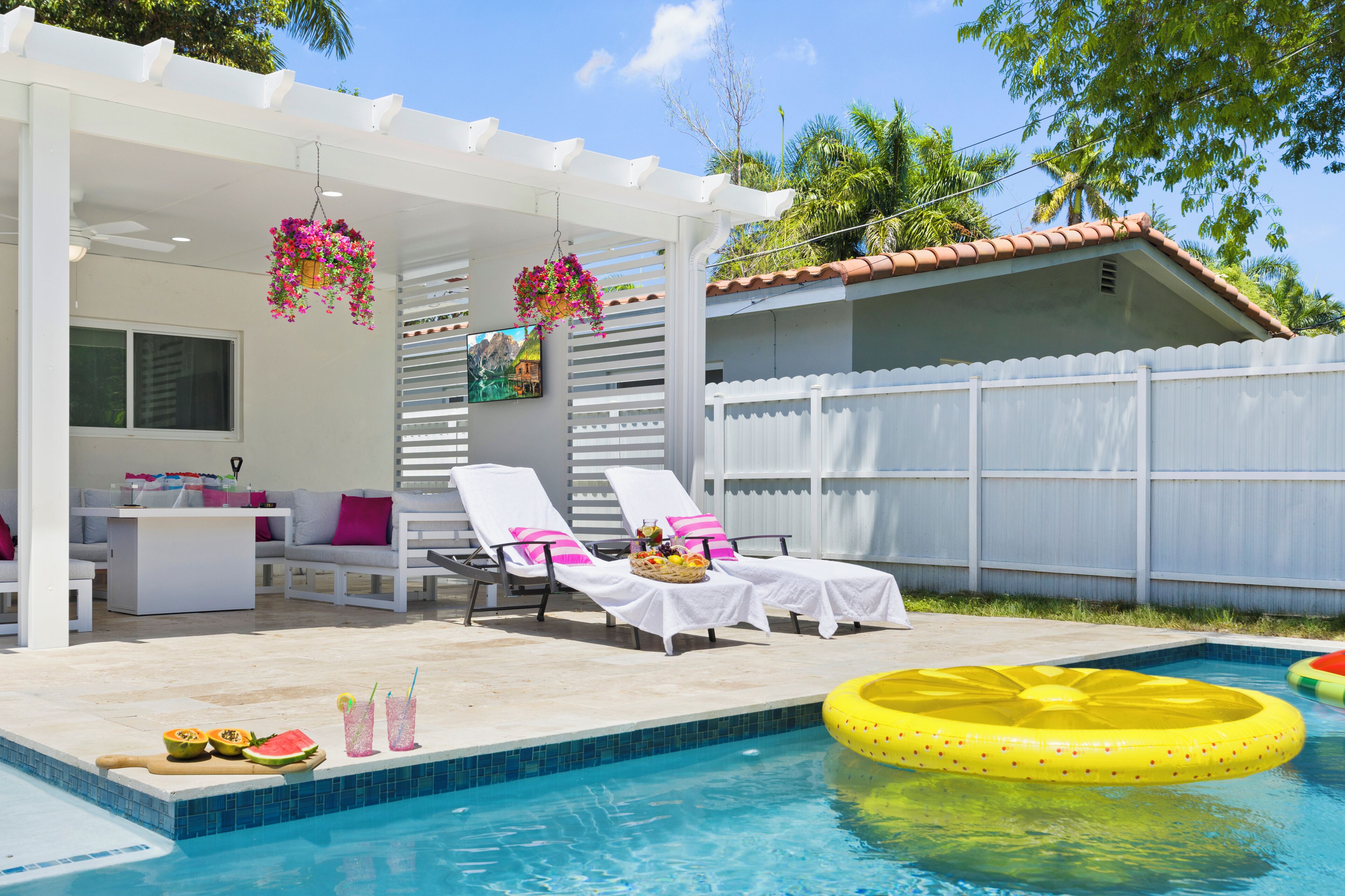 A poolside area with lounge chairs, a dining table, and a hanging flower basket.