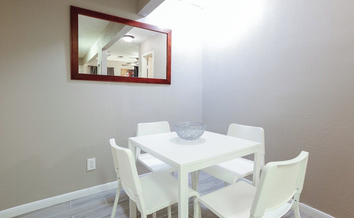 A dining area with a white table and chairs, a glass bowl on the table, and a mirror on the wall.