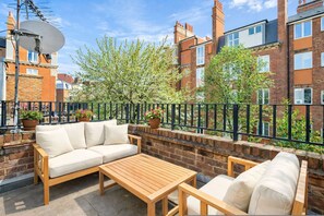 A patio with a sofa, table, and potted plants. - Chelsea Townhouse Garden Roof Terrace Pet Friendly (London)