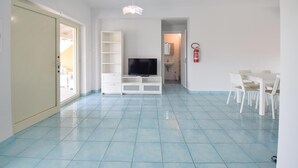 Amplia sala de estar con televisión, muebles blancos y extintor.