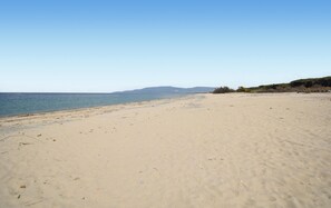 Ein weiter Sandstrand mit freiem Blick auf das Meer und sanfte Hügel in der Ferne.